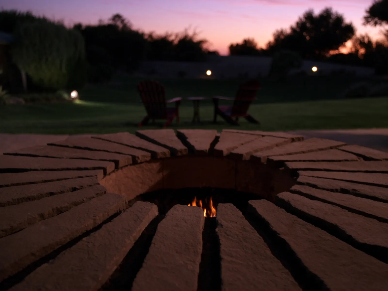 Round fire-pit pad of irregular Arizona Buckskin sandstone flagstone with low flames at dusk