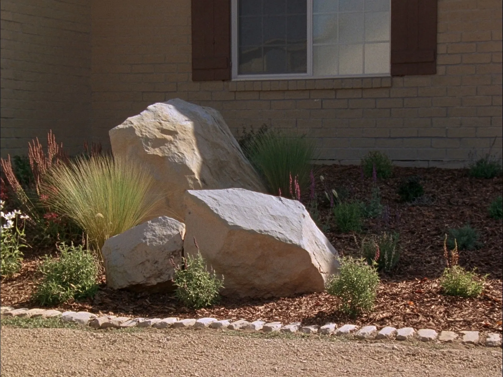 Cluster of Texas Country Cobble accent boulders in a mulched front yard bed with native Texas plantings at a brick Texas home